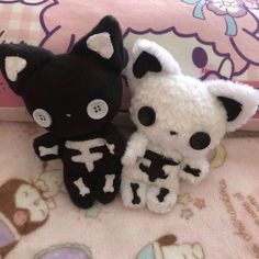 two black and white stuffed animals sitting next to each other on a pink bedspread