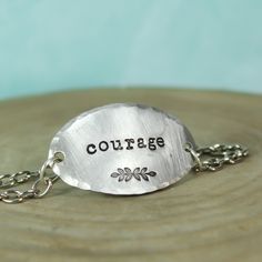 It only takes one little word to touch someone’s heart.This inspirational word bracelet makes a memorable gift idea that your recipient is sure to cherish. Artistically designed to perfection, it features a large oval shaped pendant stamped with the word “courage” and a whimsical leaf motif. Suspended from coordinating chain, it features a delicately hand hammered edge that adds layers of character. When worn, it caresses the top of your wrist beautifully and is sure to become a treasured access Stamped Metal Jewelry, Sterling Silver Hand-stamped Bracelet, Symbolic Stamped Silver Bracelets, Inspirational Adjustable Stamped Bracelets, Meaningful Stamped Adjustable Bracelet, Inspirational Hand Stamped Bracelet, Metal Stamping Kit, Custom Engraved Bracelet, Hand Stamped Metal