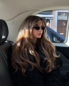 a woman sitting in the back seat of a car with long hair and sunglasses on