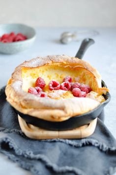 a pie with raspberries in it sitting on top of a black plate next to a bowl