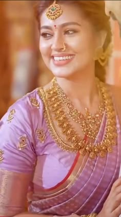 a woman in a pink and gold sari with jewelry on her neck, smiling at the camera