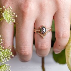 a woman's hand with a ring on it and flowers in the foreground