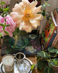 a table topped with flowers and two cups filled with water next to books on top of a wooden table