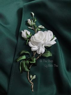 a white rose with green leaves on a dark green satin background