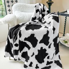 a black and white cow print blanket sitting on top of a chair next to a window