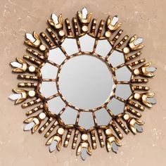 a round mirror with gold and silver decorations on the bottom, in front of a beige wall