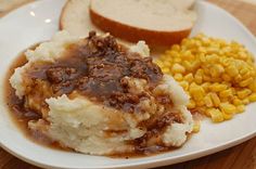 a white plate topped with mashed potatoes, meat and gravy next to corn