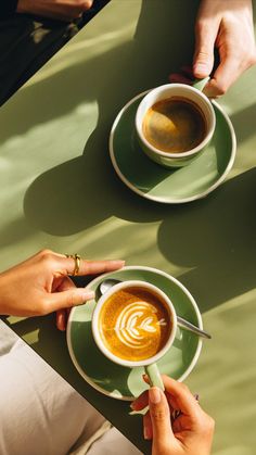 two people sitting at a table with cups of coffee in front of them, one holding a spoon