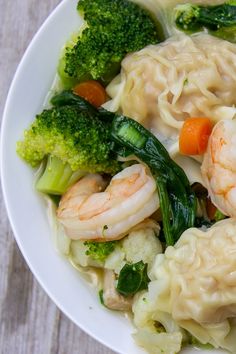 a white plate topped with dumplings and broccoli next to carrots on top of a wooden table