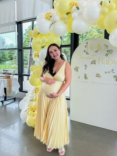 a pregnant woman in a yellow dress standing under a balloon arch with flowers on it