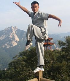 a man standing on top of a wooden rail doing a trick in the air with his arms outstretched