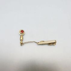 This very cool  goldtone metal tie clip or clasp is in very good condition with a stick pin attachment with a cranberry glass bead in a metal swirl . The stickpin measures 1 5/8ths inch high and  1/2  inches wide. It is attached to a tie clip by a 1 1/4 inch chain. It is marked HICKOK, USA on the back.   This will arrive in a lovely gift box for stellar gift giving or safe storage.  It would make a fabulous groomsman gift. If you like the older men's accessories, vintage costume jewelry, old sil Vintage Yellow Gold Pins For Formal Occasions, Classic Gold Pins For Formal Occasions, Antique Gold Pins For Formal Occasions, Elegant Clip-on Brooches For Formal Occasions, Vintage Adjustable Ties For Gifts, Gold Clip-on Cufflinks For Business, Gold Clip-on Cufflinks Gift, Ascot Ties, Vintage Screw Back Clip-on Earrings For Gift