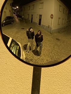 two people standing in front of a mirror on the side of a road at night