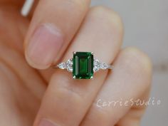 a woman's hand holding an emerald and diamond ring