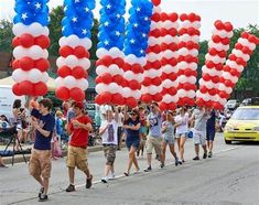 people are walking down the street with red, white and blue balloons in the shape of an american flag