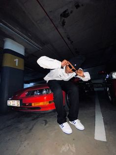 a man sitting on top of a red car in a parking garage