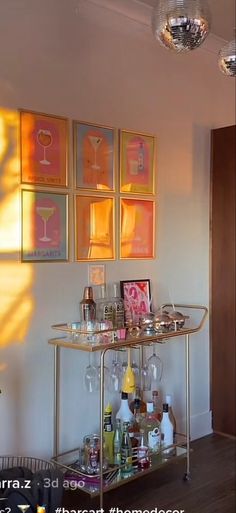 a bar cart with wine glasses on it in front of some pictures and artwork hanging on the wall