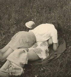 an old black and white photo of two people laying in the grass