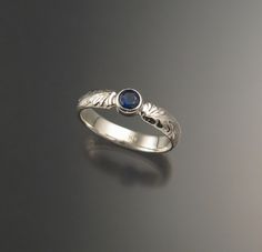 a silver ring with a blue stone in the center and leaves on it's side