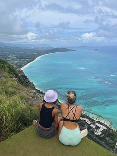 two women sitting on top of a hill overlooking the ocean