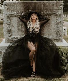 a woman in a black dress and hat sitting on a grave