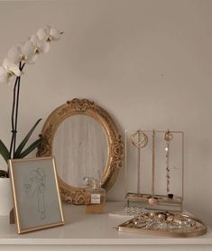 a white desk topped with a mirror next to a vase filled with flowers and jewelry