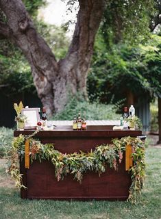 an outdoor bar is decorated with greenery and bottles of booze on the table