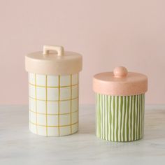 two ceramic containers sitting on top of a marble counter next to each other, one with a lid and the other with a handle