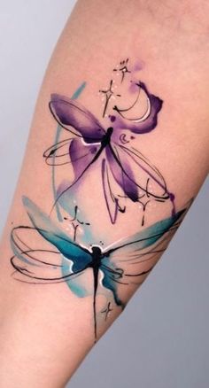 a woman's arm with watercolor tattoos on it and an image of a dragonfly