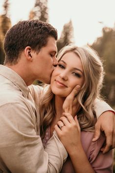 a man and woman kissing each other in front of the camera with trees behind them