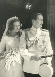 an old black and white photo of a man and woman dressed in wedding attire standing next to each other