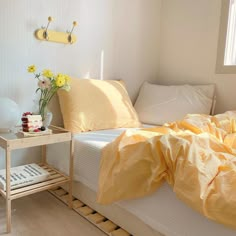 a bed with yellow sheets and pillows in a bedroom next to a small end table