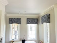 a kitchen with white cabinets and black patterned roman shades