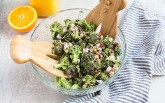 a glass bowl filled with broccoli, onions and oranges next to a cutting board