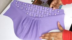 a woman is working on a piece of purple material with buttons and pearls in it