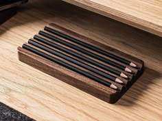 several pencils are lined up in a wooden holder next to a cell phone on a table