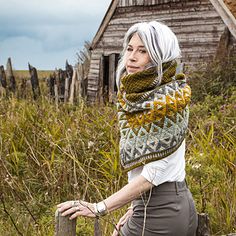 a woman with white hair is leaning on a fence in front of an old house