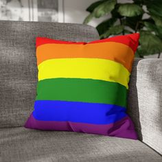 a rainbow colored pillow sitting on top of a gray couch next to a potted plant