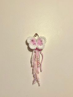 a pink and white crocheted keychain hanging on a wall with beads