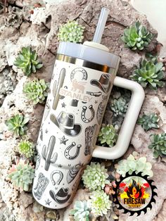 the tumbler is sitting next to some succulents and rocks with an image of cowboys on it