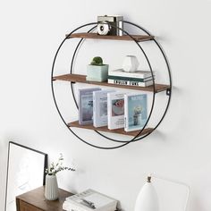 a round metal shelf with books on it in the corner next to a white wall