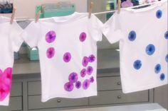 three t - shirts hanging on a clothes line with pink and blue flowers painted on them