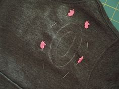 some pink pins sticking out of the back of a gray t - shirt that is being sewn