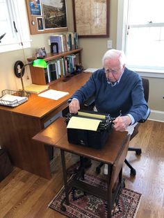 an old man sitting at a desk with a typewriter