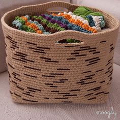 a basket filled with crocheted fabric on top of a white couch next to a pillow