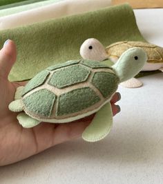 a hand holding a small stuffed turtle next to two smaller turtles on a table with green towels