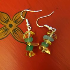 two pairs of earrings with green and yellow beads hanging from them on a red surface