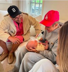 three people sitting on a couch with a baby in their lap and one holding a bottle