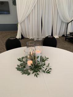 some candles are sitting on top of a round table with greenery in front of it