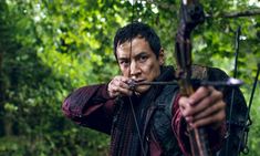 a man holding a bow and arrow in his hand while looking at the camera with an intense look on his face